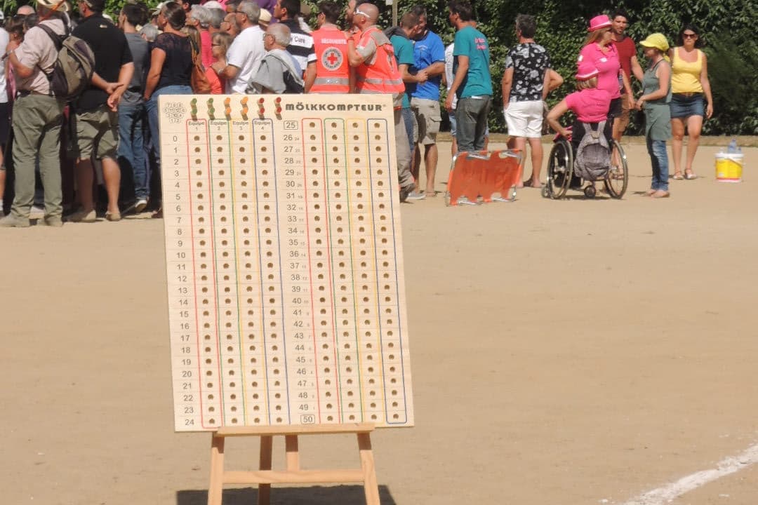 Een groot houten scorebord met pinnen op een ezel bij een Mölkky-toernooi, met kolommen gaatjes genummerd van 0 tot 50 voor vier teams.