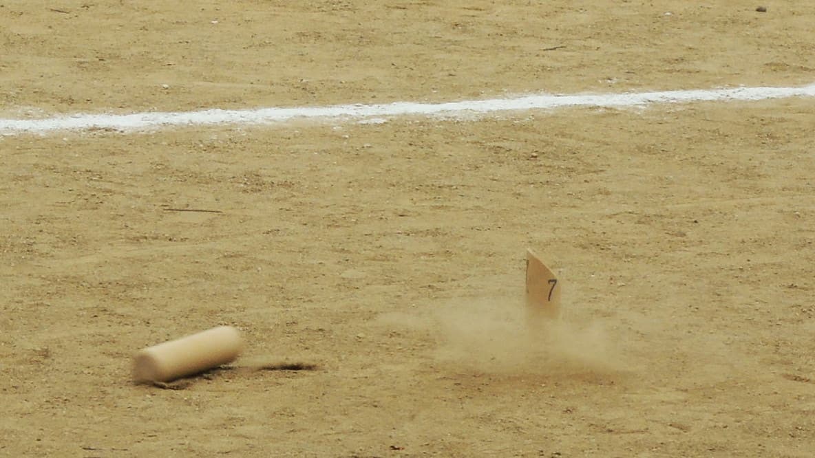 A numbered pin going over in a cloud of dust on a sand court, the thrown mölkky already lying on the ground beside it.